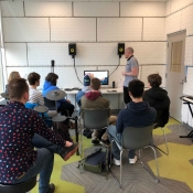 An image of people standing in the sound studio learning about how the equipment works.