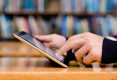 Teen Tech Volunteers Closeup of hands holding a tablet with books in the background